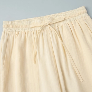 Detail of light beige elastic waist pants featuring drawstring and vertical pleat texture