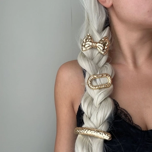Hammered gold metal hair clips set including bow and oval shapes on braided blonde hair