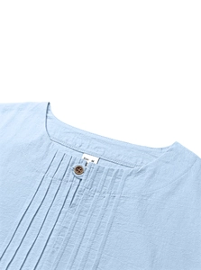 Détail du col d'une chemise en coton bleu clair avec des plis verticaux et bouton en bois