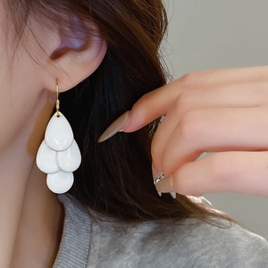 Detail of layered white teardrop petal earrings with golden hooks worn by model