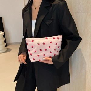 Pink corduroy strawberry print clutch bag held by model with minimalist design