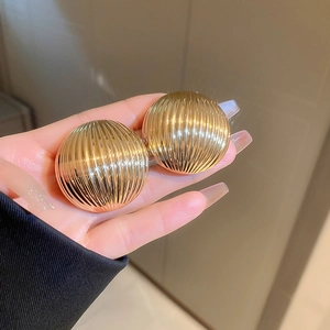 Detailed close-up of golden chunky semi-circle earrings with vertical striped metal texture