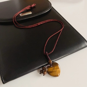 Detail of woven rope necklace featuring a heart-shaped tiger eye stone pendant