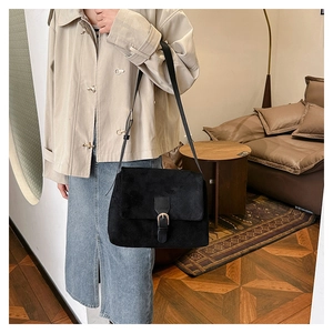 Detail of black faux suede saddle bag with adjustable strap and silver metal buckle closure