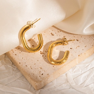 Detail of 18k gold plated chunky U-shaped hoop earrings on elegant textured stone background