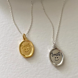 Close-up of gold and silver Smile necklaces with wax seal style oval pendants