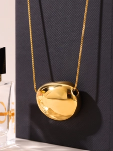 Detailed view of polished 18k gold plated bean pendant necklace on a textured background