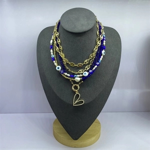 Detail of layered gold necklace with heart pendant, blue beads, and evil eye charm