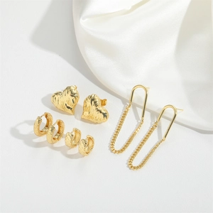 Luxury gold heart earrings and textured hoops set displayed on elegant white silk