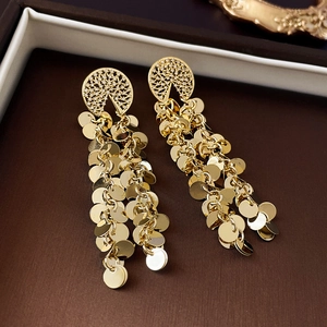Detailed close-up of golden tassel earrings with metal discs in a dark jewelry box