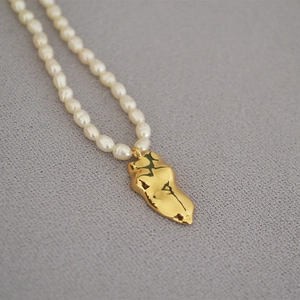 Macro shot of freshwater pearl necklace with an artistic golden body pendant