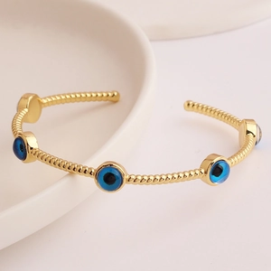 Detail of gold-plated open bangle with blue evil eye charms and spiral texture
