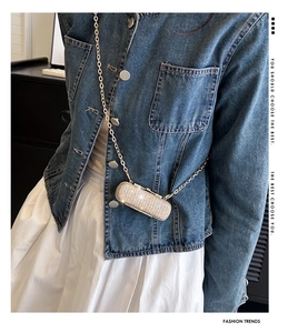 Detail of a mini rhinestone crossbody bag with gold chain worn over a denim jacket
