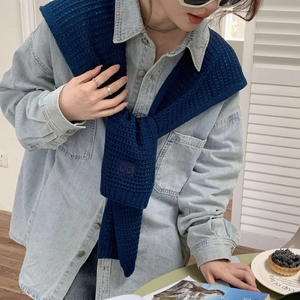 Detail of navy knit shawl with DD logo embroidery worn over a denim shirt