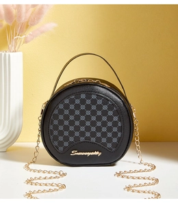 Détail d'un sac rond en cuir noir avec motif trèfle et bandoulière en chaîne dorée