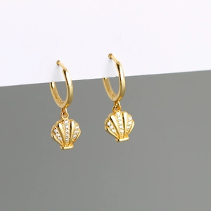 Close-up of gold hoop earrings featuring shell pendants with clear zircon micro-inlay