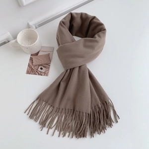 Flat lay of khaki faux cashmere scarf with fringes next to a mug on white surface