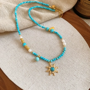 Détail du collier de perles turquoise avec pendentif soleil doré sur tissu en lin