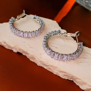 Detailed view of silver hoop earrings with square zircon stones on stone surface