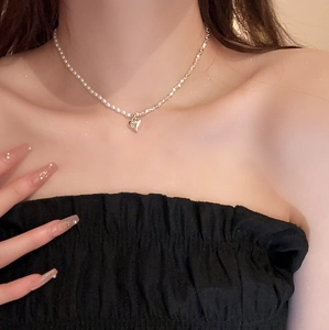 Gros plan du collier en perles et chaîne argentée avec pendentif cœur porté
