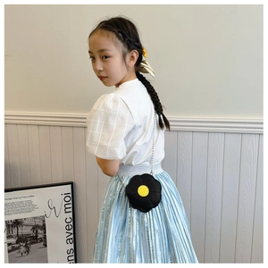 Girl wearing a black flower-shaped shoulder bag with a yellow center and metal chain strap