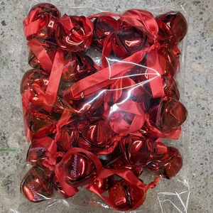 Close-up of red Christmas bells with Believe engraving and ribbons in bulk packaging