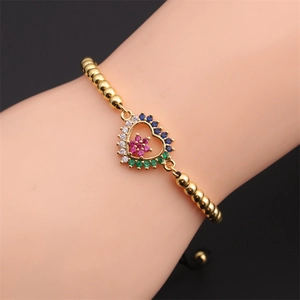 Macro shot of gold beaded bracelet featuring a colorful zircon heart charm with floral detail