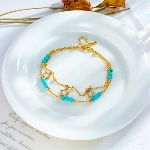 Double-layered gold anklet with blue beads and white star pendant on a white plate