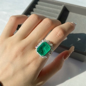 Detail of emerald-cut green gemstone ring with sparkling diamond halo setting