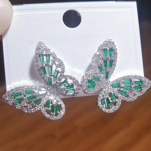 Detail of silver butterfly stud earrings with emerald green rectangular cut zircon