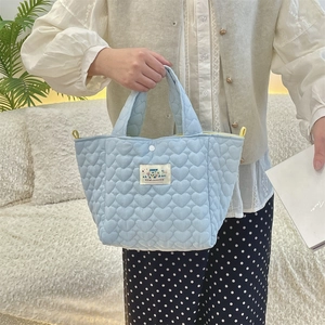Detail of light blue quilted handbag featuring heart stitching and Happy label