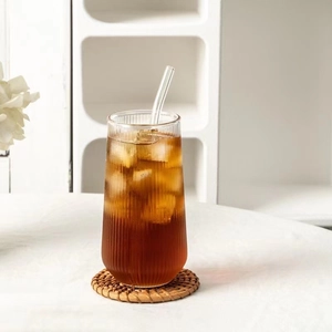 Close-up of tall ribbed glass with straw and iced coffee on a woven coaster