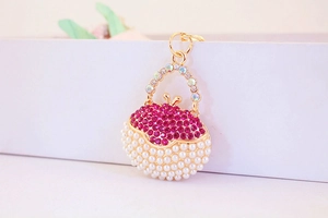 Detail showing handbag-shaped keychain with pink rhinestones and white pearls on gold metal