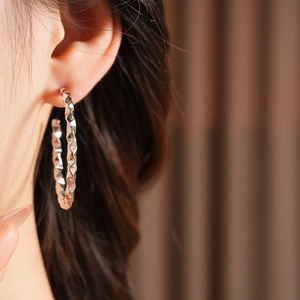 Close-up of a silver geometric hoop earring with diamond-cut texture on a model