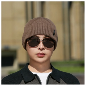 Detail of a brown knit beanie featuring a side logo tag and warm ribbed texture