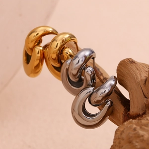 Macro shot of 18K gold and silver geometric C-shaped hoop earrings on natural wood stand