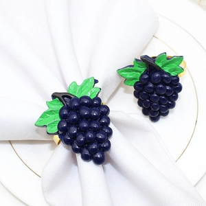 Detail showing grape-shaped napkin rings with purple fruits and green leaves on white linen