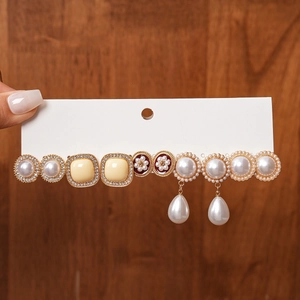 Detailed set of vintage earrings featuring pearls and rhinestones on a handheld display board