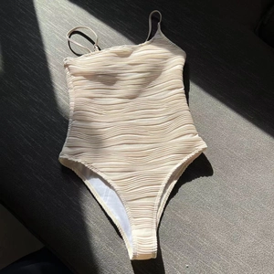 Detail showing the textured wavy fabric and minimalist ivory white one-piece swimsuit