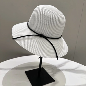 Détail d'un chapeau de soleil tressé blanc avec ruban noir sur un support métallique