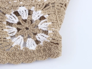 Close-up of beige crochet knit fabric with white floral embroidery and hollow textures
