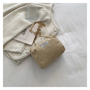 Detail of khaki corduroy mini bag with gold chain strap and fashion label on a table