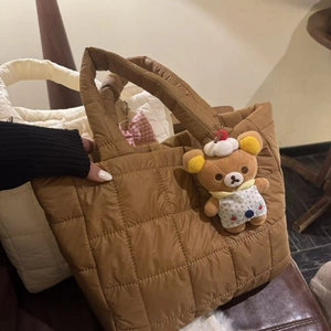 Close-up of caramel quilted tote bag featuring a cute teddy bear plush charm detail