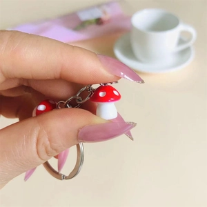 Handheld view of resin mushroom keychains featuring red caps with white spotted details