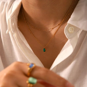 Detail of 18k gold double-layer necklace with green emerald-cut zircon on linen shirt