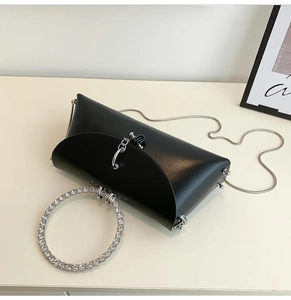 Detail of a black geometric evening bag with a rhinestone ring handle and silver chain