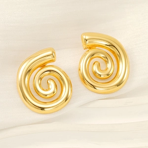 Gros plan de boucles d'oreilles spirales dorées sur soie montrant la texture métal minimaliste