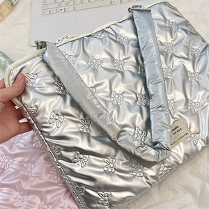 Detail of silver quilted laptop sleeve with bow embroidery held next to a computer