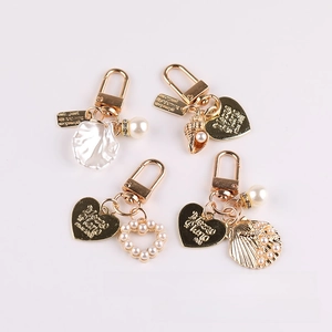 Detail view of gold keychains with white faux pearls and heart charms on white background