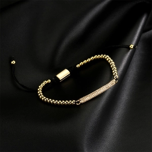 Makroaufnahme von Goldperlen und Zirkonia-Stab an schwarzem geflochtenem Armband